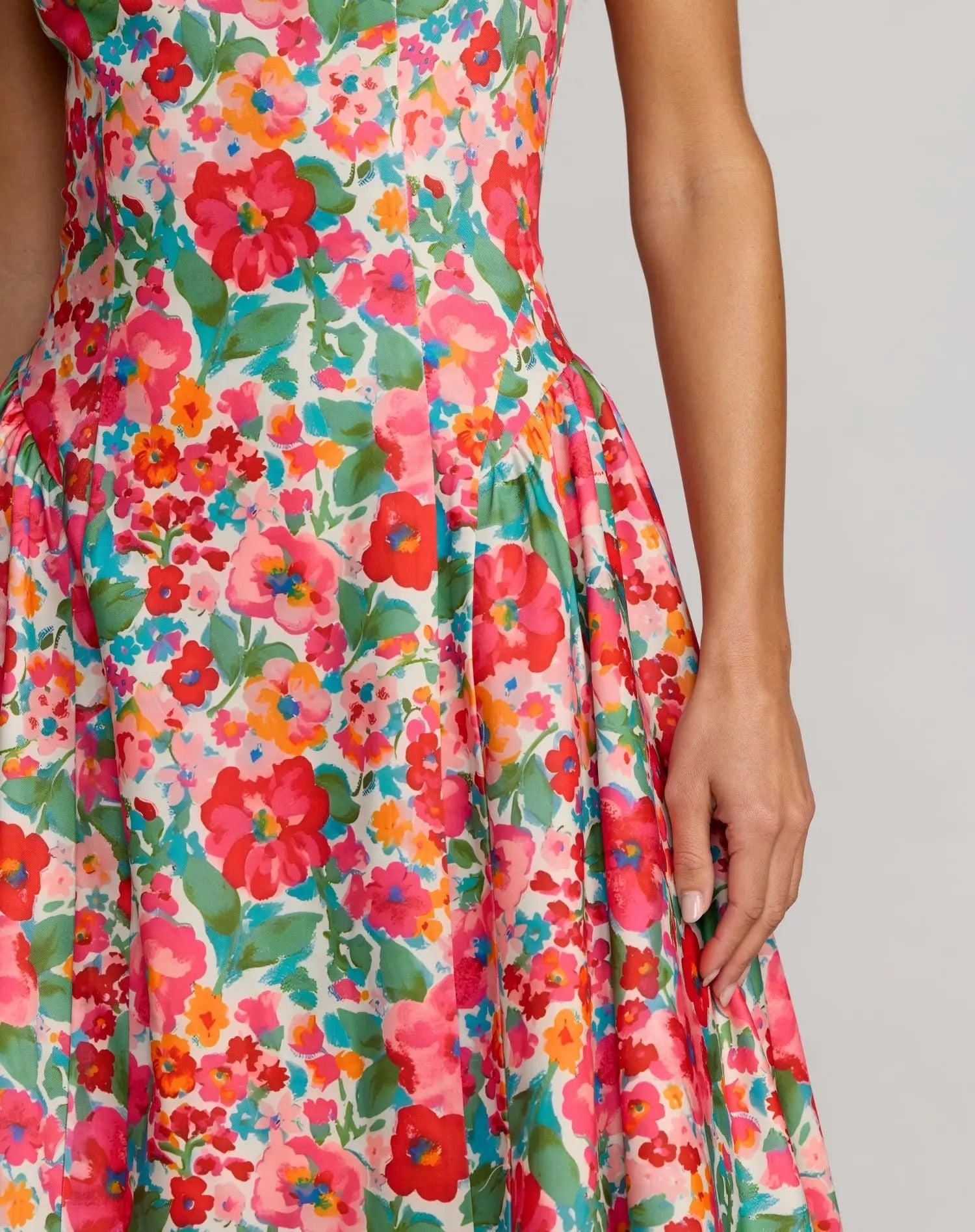 A person wearing the Floral Midi Wedding Guest Dress: Mac Duggal 37155, featuring a vibrant red, pink, and green floral print in an A-line midi silhouette, stands against a plain light gray background.